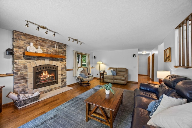 living area featuring a fireplace, a textured ceiling, wood finished floors, track lighting, and baseboards