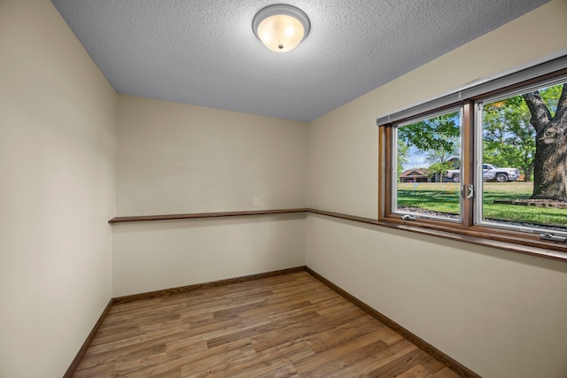empty room with healthy amount of natural light, wood finished floors, baseboards, and a textured ceiling