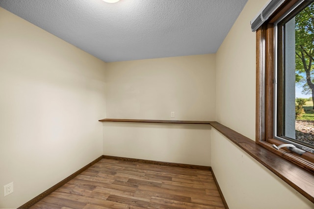 spare room with wood finished floors, a textured ceiling, and baseboards