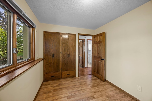 unfurnished bedroom with light wood-style floors, baseboards, and a textured ceiling