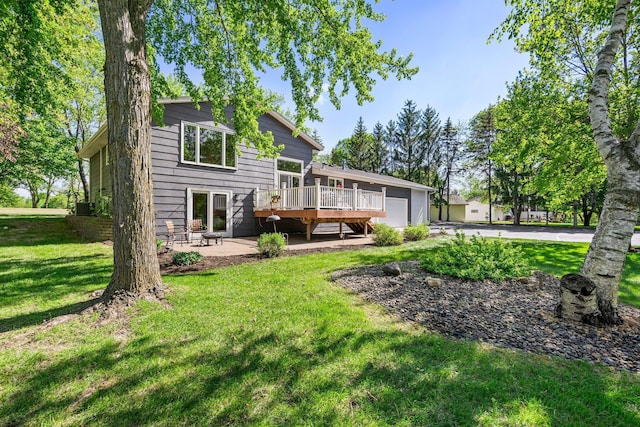 back of property featuring a lawn, a deck, an attached garage, driveway, and a patio area