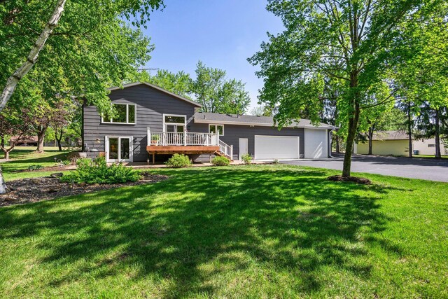 split level home with a deck, driveway, an attached garage, and a front lawn