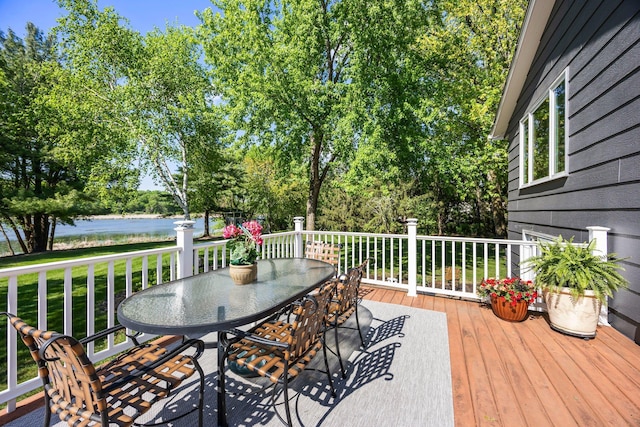 wooden deck featuring outdoor dining area, a water view, and a lawn