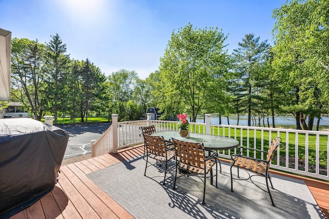 deck with a water view, outdoor dining area, grilling area, and view of scattered trees