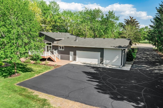 view of front facade with roof with shingles, asphalt driveway, an attached garage, and a wooden deck