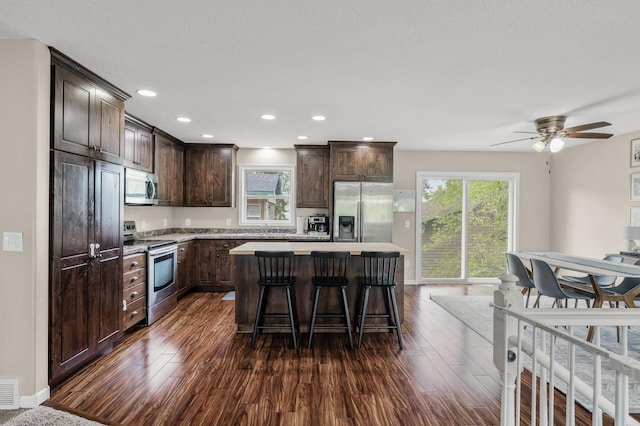 1002 8th Ave N, Princeton, MN 55371 - kitchen with stainless steel appliances, dark brown cabinets, a kitchen island, dark wood-style floors, and a kitchen breakfast bar