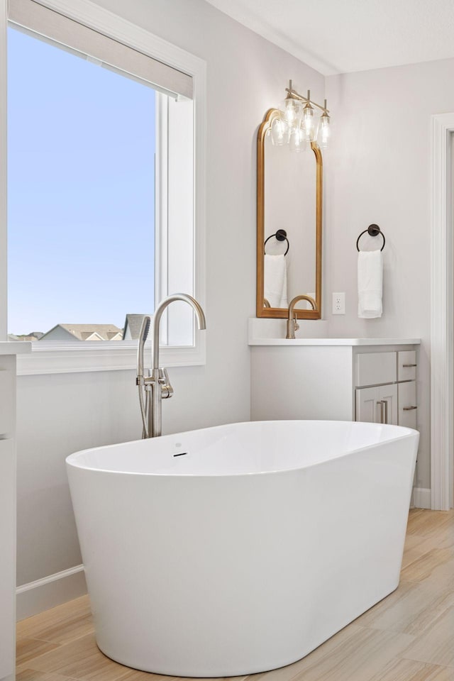 bathroom featuring wood finished floors, a freestanding tub, and baseboards