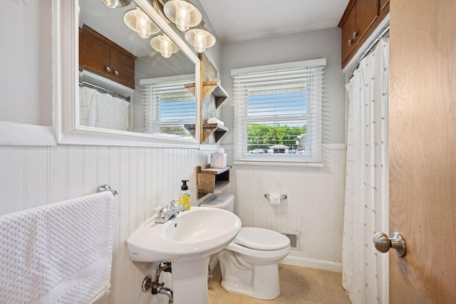bathroom with toilet, wainscoting, and a shower with shower curtain