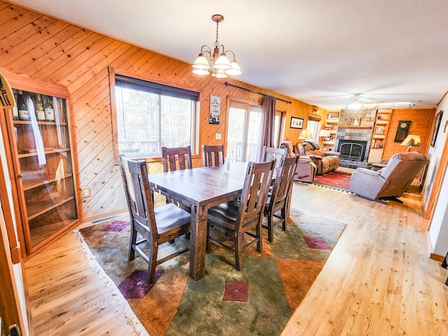 1910 Longwood Point Rd NE, Outing, MN 56662 - dining area featuring wooden walls, wood finished floors, a ceiling fan, a fireplace with raised hearth, and a chandelier