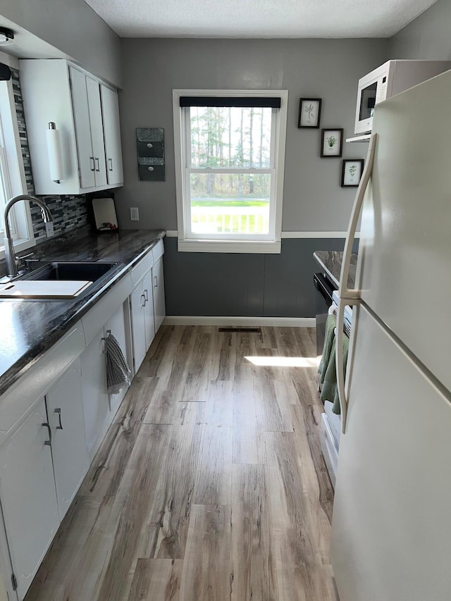 603 Main Ave N, Roseau, MN 56751 - kitchen with white appliances, a sink, dark countertops, white cabinets, and light wood-type flooring