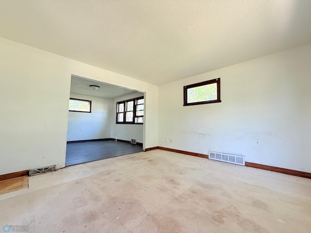 spare room with baseboards, unfinished concrete floors, and a textured ceiling