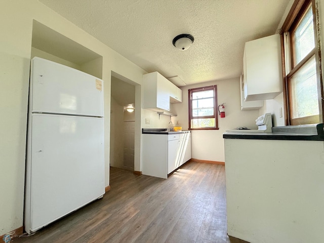 kitchen featuring freestanding refrigerator, wood finished floors, a textured ceiling, white cabinetry, and baseboards