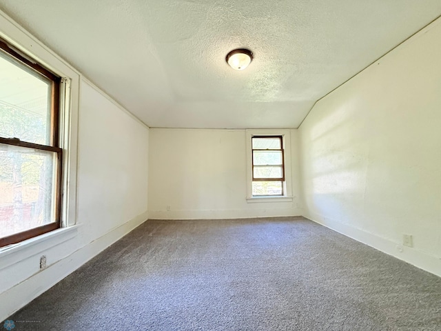 empty room with a textured ceiling, lofted ceiling, carpet, and baseboards