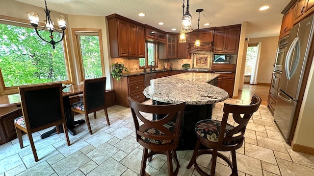 kitchen featuring appliances with stainless steel finishes, a sink, a center island, stone tile flooring, and backsplash