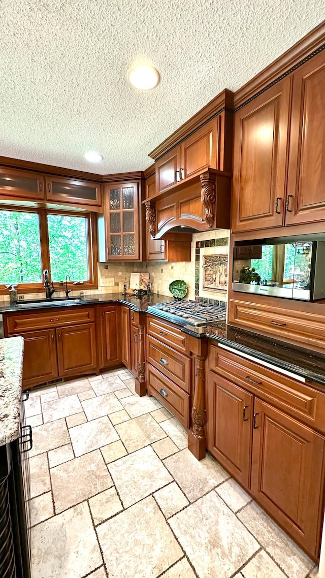 kitchen with stainless steel appliances, a textured ceiling, a sink, brown cabinets, and stone tile flooring