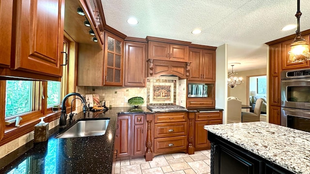 kitchen featuring a sink, stainless steel appliances, dark stone counters, backsplash, and a chandelier