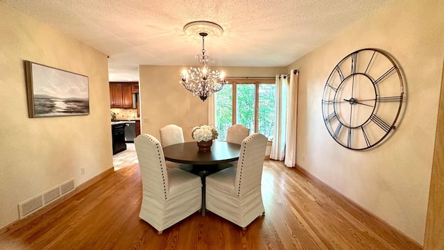 dining area featuring a chandelier, light wood-style flooring, a textured ceiling, and baseboards
