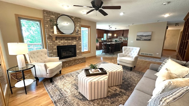 living area featuring a ceiling fan, light wood finished floors, a textured ceiling, a brick fireplace, and baseboards
