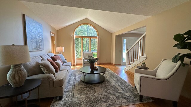 living room featuring wood finished floors, vaulted ceiling, stairs, and a textured ceiling
