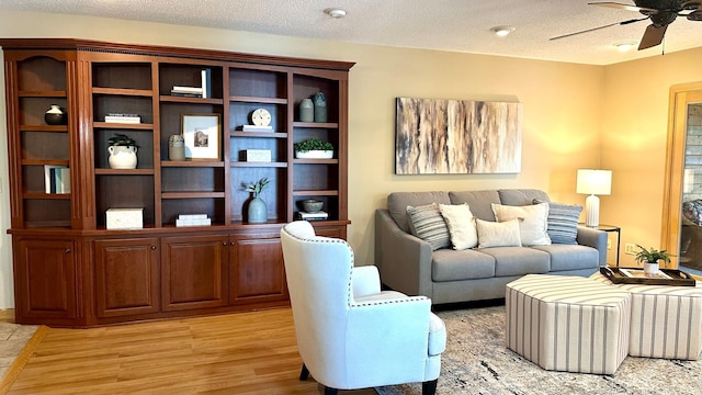 living area featuring a ceiling fan, light wood-style flooring, and a textured ceiling