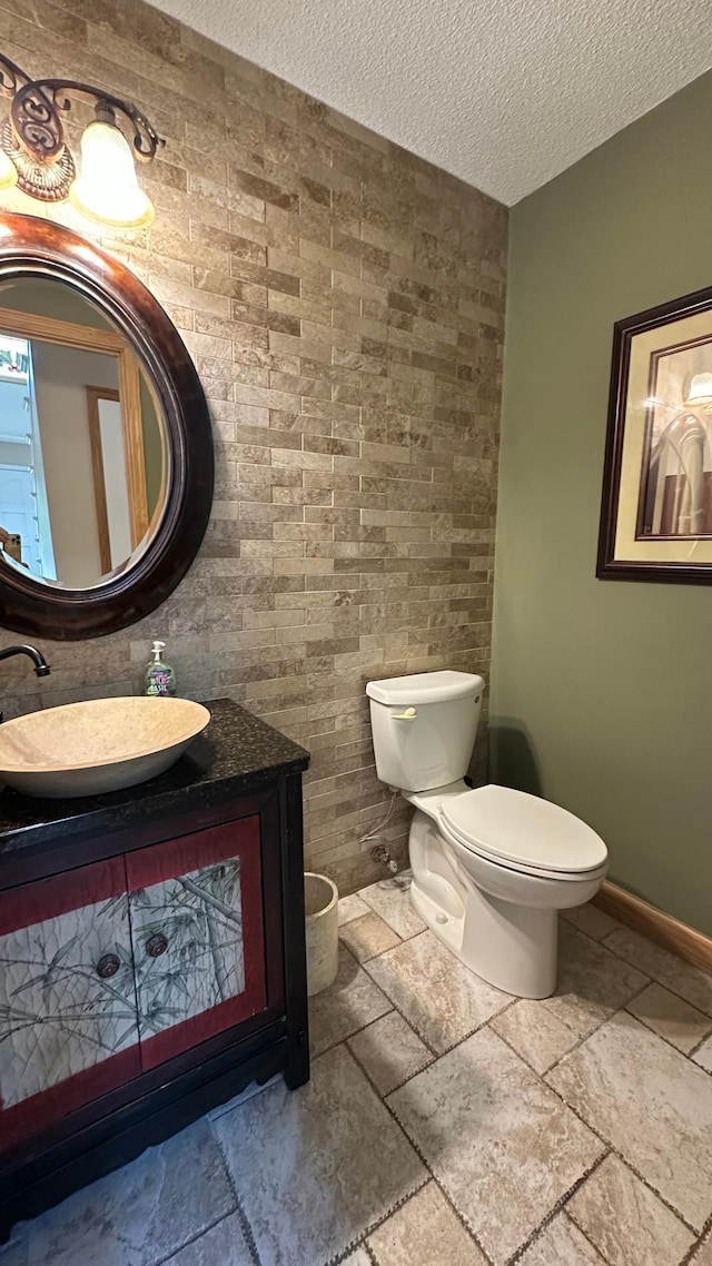 bathroom featuring stone tile floors, toilet, vanity, a textured ceiling, and baseboards