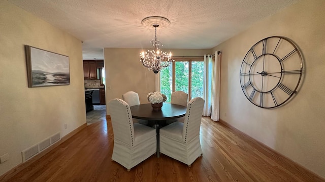 dining area featuring light wood-style floors, a chandelier, a textured ceiling, and baseboards