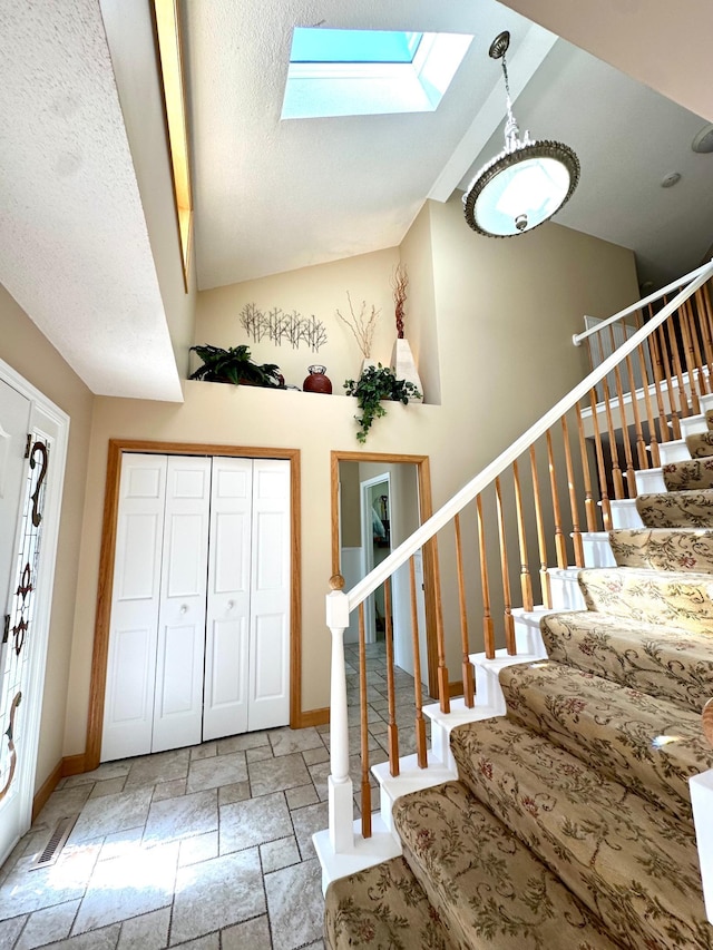 foyer with a skylight, stone tile flooring, lofted ceiling, stairs, and baseboards