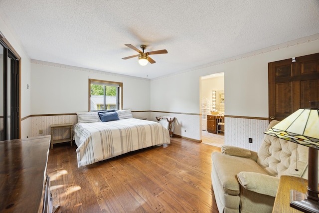 3704 Milton St N, Shoreview, MN 55126 - bedroom featuring wainscoting, light wood-style floors, a textured ceiling, ceiling fan, and ensuite bathroom