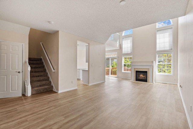 1353 White Oak Dr, Chaska, MN 55318 - unfurnished living room with light wood-type flooring, stairway, baseboards, a glass covered fireplace, and a textured ceiling