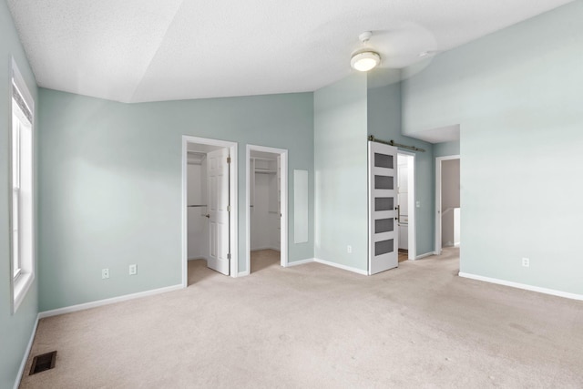 1353 White Oak Dr, Chaska, MN 55318 - unfurnished bedroom featuring vaulted ceiling, light carpet, baseboards, a walk in closet, and a barn door