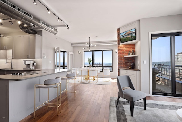 kitchen featuring light wood finished floors, a sink, dark countertops, black electric cooktop, and backsplash