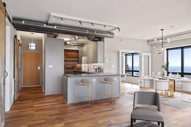 kitchen with a barn door, light wood-style floors, a peninsula, pendant lighting, and a sink