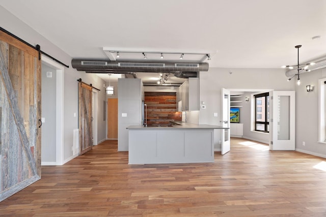 kitchen featuring a barn door, light wood finished floors, rail lighting, white cabinetry, and hanging light fixtures