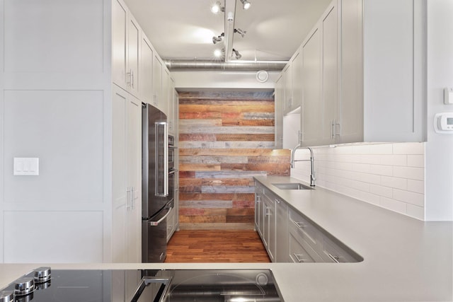 kitchen with a sink, decorative backsplash, light countertops, high end fridge, and wood finished floors