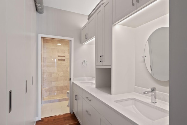 bathroom with a tile shower, toilet, double vanity, and wood finished floors