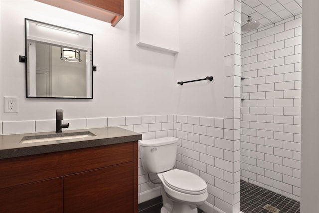 full bath with toilet, tiled shower, vanity, tile walls, and wainscoting