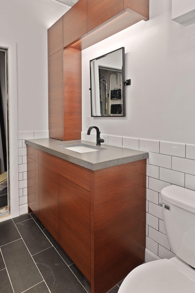 half bathroom featuring toilet, tile walls, vanity, wainscoting, and tile patterned floors