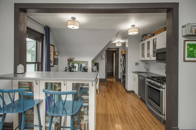 kitchen featuring appliances with stainless steel finishes, a kitchen breakfast bar, white cabinetry, a peninsula, and glass insert cabinets