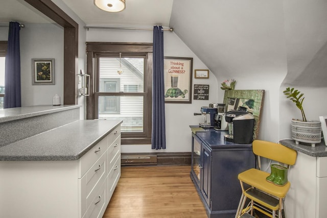 kitchen with white cabinets, light wood-style flooring, vaulted ceiling, and dark countertops