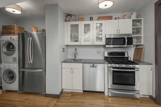 kitchen featuring stainless steel appliances, a sink, stacked washer / drying machine, and white cabinets