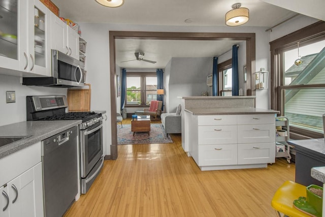kitchen with stainless steel appliances, a ceiling fan, white cabinetry, light wood-style floors, and glass insert cabinets