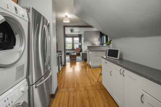 kitchen featuring appliances with stainless steel finishes, estacked washer and dryer, light wood-style floors, white cabinetry, and dark countertops