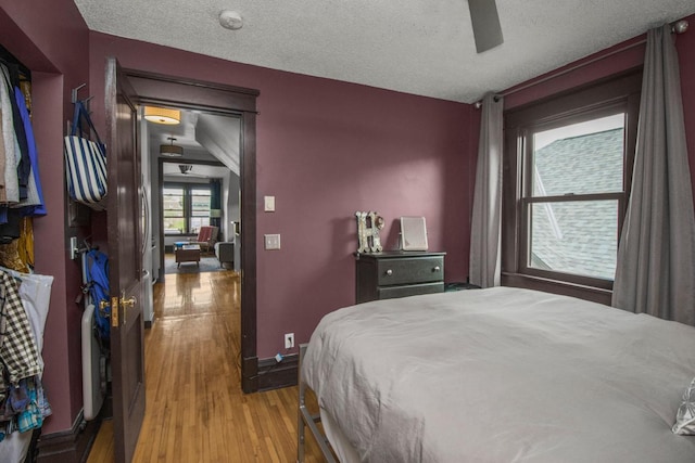 bedroom featuring wood finished floors, a textured ceiling, baseboards, and ceiling fan