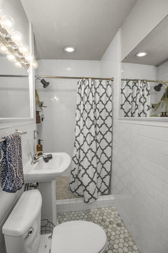 bathroom with a textured ceiling, toilet, tiled shower, tile walls, and tile patterned floors