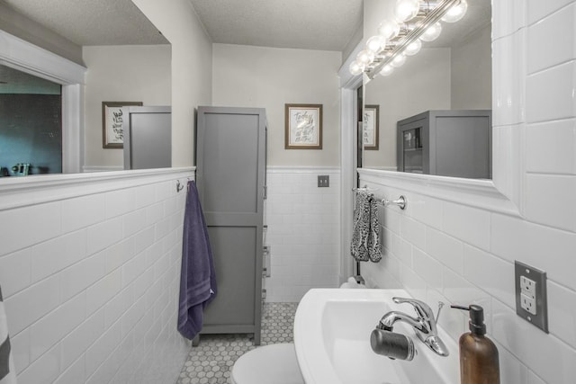 bathroom with tile walls, tile patterned floors, a textured ceiling, wainscoting, and toilet