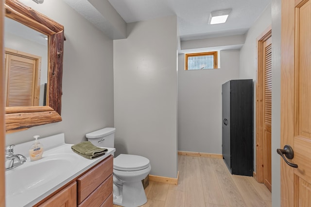 bathroom with wood finished floors, toilet, vanity, a closet, and baseboards