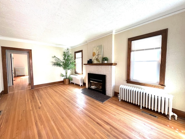 living area featuring radiator heating unit, a textured ceiling, crown molding, light wood-style flooring, and a fireplace