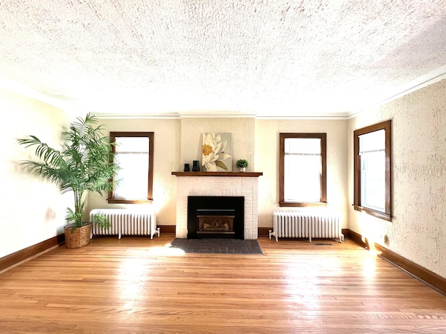 living room with radiator, plenty of natural light, wood finished floors, crown molding, and a textured ceiling