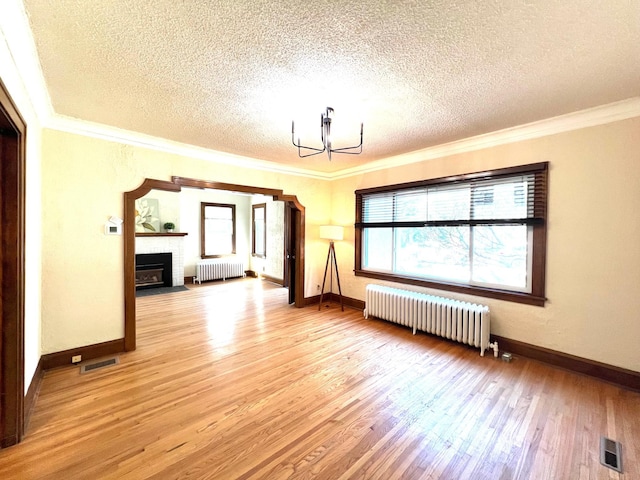 unfurnished living room featuring radiator heating unit, a textured ceiling, a chandelier, light wood-type flooring, and ornamental molding