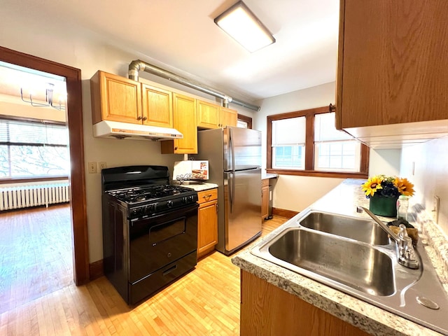 kitchen with black range with gas stovetop, under cabinet range hood, radiator heating unit, freestanding refrigerator, and a sink